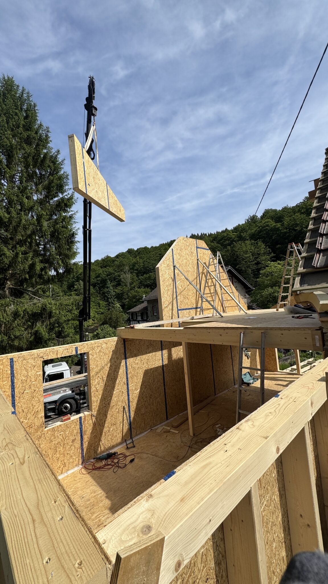 Holzrahmenbauwand hängt an einem Kran und wird aufgestellt für einen Anbau