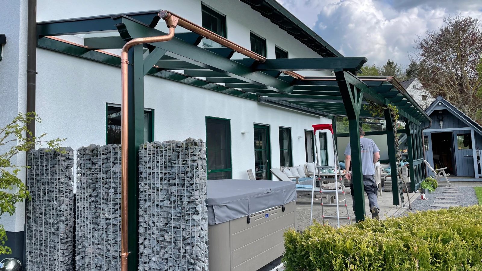 Grüne Pergole mit VSG über einer Terrasse.